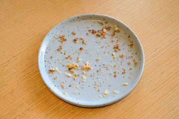 Top view of an empty gray ceramic plate with bread crumbs and food remains on a wooden table in natural light. Perfect for lifestyle blogs, restaurant ads, or food background designs