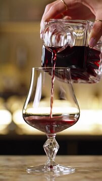 Opulent cinematic mcu video: refined hand slowly decanting rich ruby-red wine into a crystal glass on a luxurious bokeh background. Soft warm studio lighting with a subtle dolly push-in, tactile