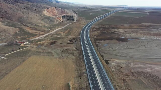 Aerial view of a ribbon of highway cutting through the arid landscape, with cars visible amidst dry fields, Tuz, Ankara, Turkiye.