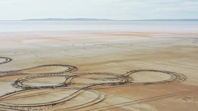 Aerial view of tire tracks creating patterns on the sandy ground against a muted backdrop, Tuz, Ankara, Turkiye.