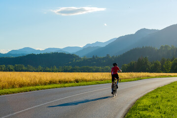 Fototapeta premium Man in sport gear riding a bicycle down the road to mountains while filming on his mobile phone