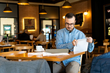 Young man reviewing financial documents in cafe