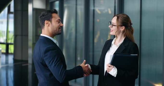 Two business people greeting with handshake in office hallway, animated smiles and expressions