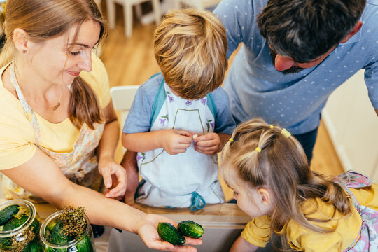 Mother helping children can cucumbers in kitchen from top view
