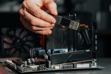 person installs an M.2 NVMe SSD into a modern motherboard connector, demonstrating the assembly of computer equipment in the process.