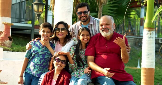 Indian family smiling on steps outdoors spending quality time together on green lawn, cheerful multi-generation portrait of grandparents, parents, and kids bonding, relaxing, enjoying leisure weekend