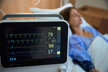 Modern heart rate monitor in hospital with female patient in background