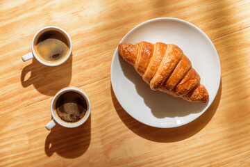 Two espresso cups and croissant in morning sun rays
