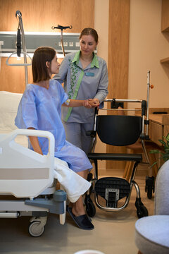 Female patient being helped by nurse from bed to wheelchair