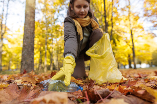 Volunteer cleaning up autumn leaves with yellow gloves and trash bag