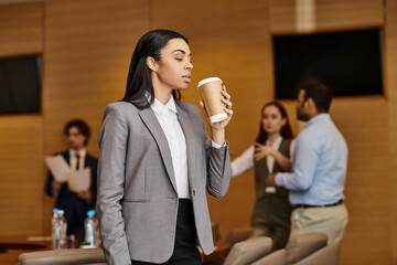 Modern office scene of a confident woman enjoying coffee while colleagues collaborate
