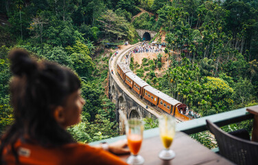 Woman watches train cross Nine Arch Bridge Sri Lanka from a cafe