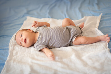 A very young infant is lying on its back on a white soft blanket, which is on a blue bedsheet. The...