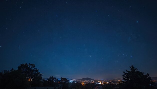Vast deep dark night sky full of bright twinkling stars. Distant city lights illuminate horizon below. Urban buildings glow softly under clear firmament. Trees form silhouettes framing calm evening