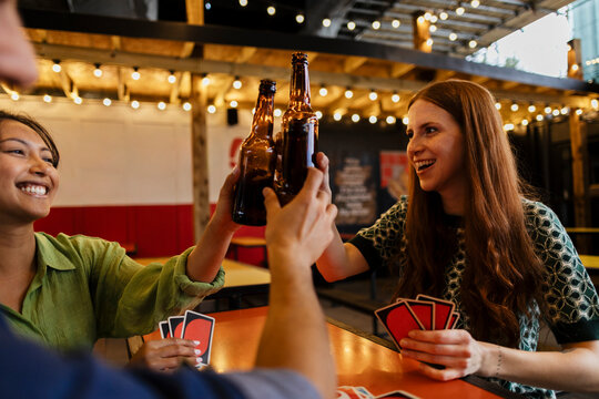 Friends toasting with beer bottles while playing cards at a bar