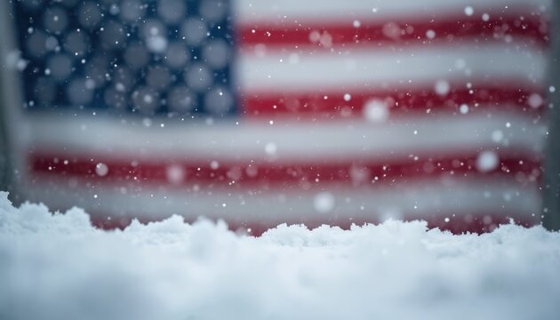 USA flag unfurls softly with falling snow creating patriotic winter scene. White snowflakes drift against blurred red white blue stripes. Cold weather national symbol evokes calm.