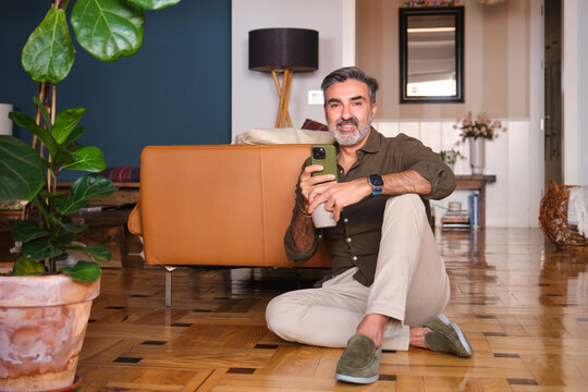 Man sitting on floor at home with coffee and phone in a relaxed mood