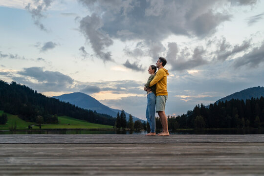 Thought mature couple hugging on jetty at dusk