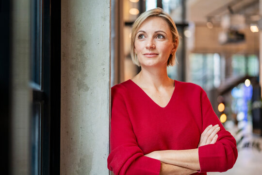 Confident businesswoman in red sweater standing in modern office - Powered by Adobe