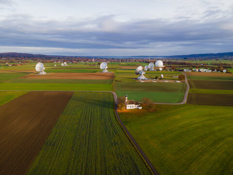 Raisting, Germany - 11 November 2025: Aerial view of the Raisting Earth Station's stark white satellite dishes puncturing the Bavarian green fields under a soft, clouded sky.