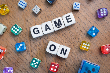 GAME ON spelt using wooden word dice with vibrant dice around set over a pale wooden tabletop background - perfect for promoting game events or fun family gatherings.