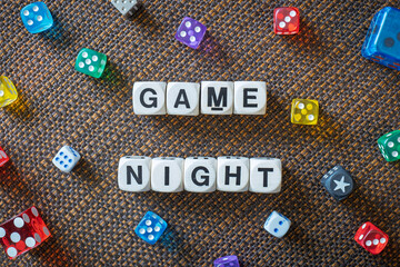 GAME NIGHT spelt using wooden word dice with vibrant dice set over a brown table cloth background - perfect for promoting game events or fun family gatherings.