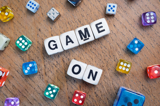 GAME ON spelt using wooden word dice with vibrant dice around set over a pale wooden tabletop background - perfect for promoting game events or fun family gatherings.