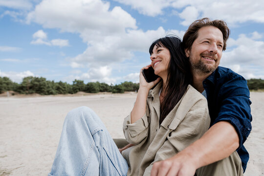 Couple relaxing outdoors on windy day woman telephoning smiling