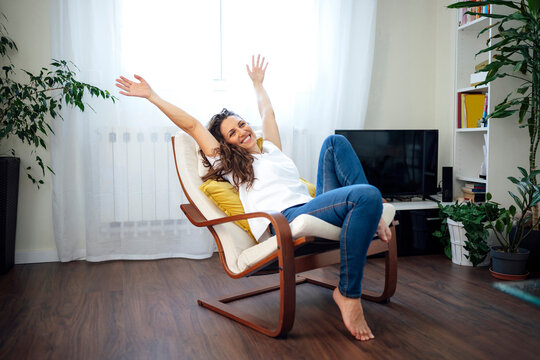 Smiling woman relaxing barefoot in armchair at home enjoying free time
