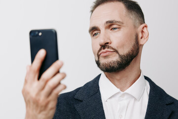 A focused business professional man, in a textured blazer, on an isolated colored background, pauses to view a smartphone, conveying thoughtful confidence and calm decision making.