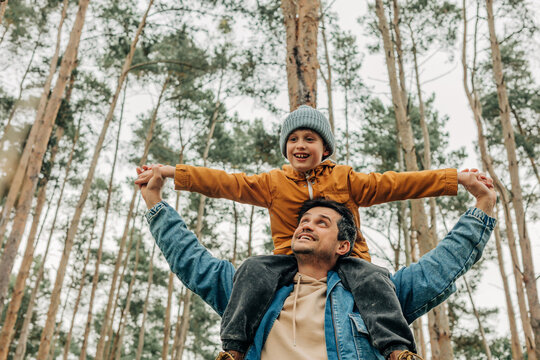 Father carrying son on shoulders in pine forest during autumn