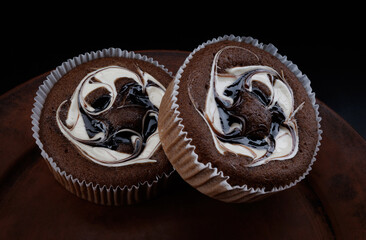 Two beautiful chocolate cakes with cream on a black background.