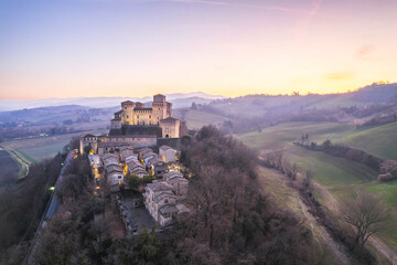 Aerial view of medieval castle and ancient village on hilltop surrounded by countryside at sunset, Torrechiara, Emilia-Romagna, Italy