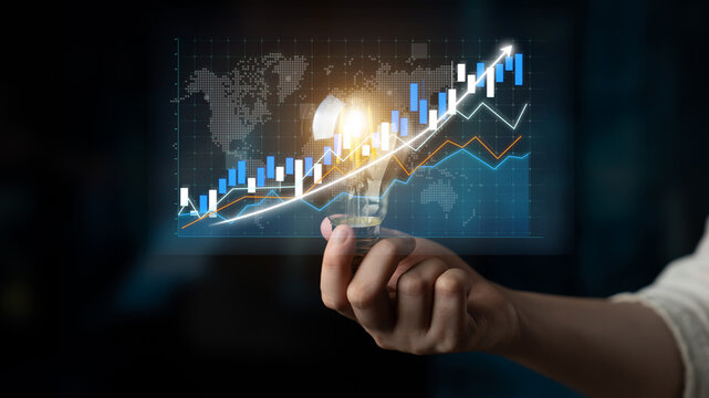 A hand holds a glowing light bulb above a digital chart displaying upward trends. This image represents innovation, growth in finance, and business strategy. Impute