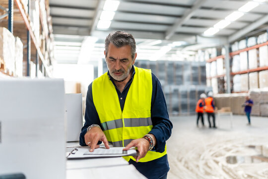 Warehouse manager wearing safety vest checking inventory list - Powered by Adobe