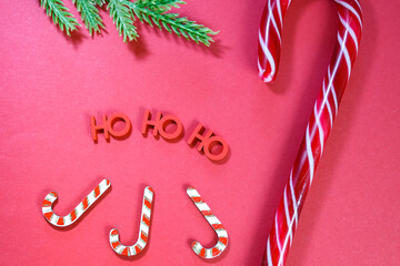 Christmas candy canes, Ho Ho Ho letters, and a pine branch on a red surface creating a festive background