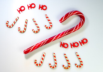 Red and white candy canes with glitter and Ho Ho Ho letters on a white surface creating a festive Christmas display