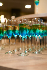 Close-up of elegant glasses filled with layered blue and yellow cocktails arranged on a wooden table. Stylish and vibrant alcoholic drinks prepared for a celebration or party, symbolizing festivity