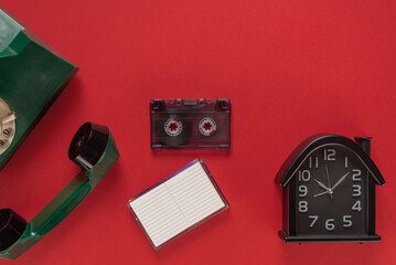 Disk phone, old watch and audio tape cassette from the past isolated on red background. Hand holding an audio cassette and an old phone, symbolizing nostalgia and a retro journey back to the past