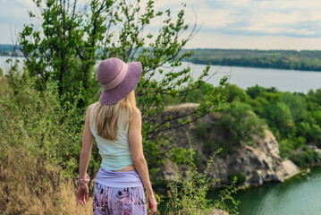 Young woman enjoying beautiful view of lake on summer day. Traveler admiring river view from cliff...