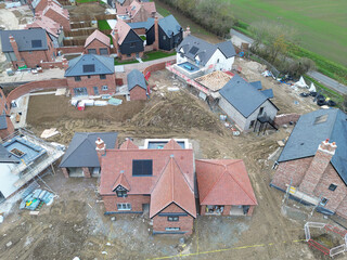 Drone view of a near completed large, detached family home on a British housing development site in rural Britain. Small houses can be seen in the background.