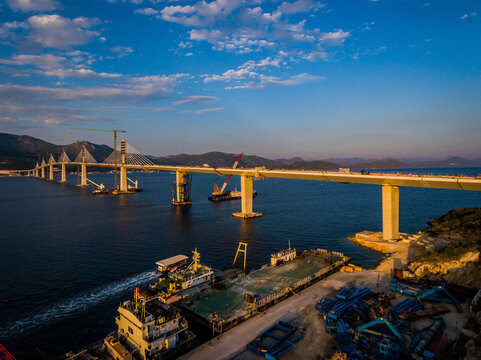 Aerial view of a long, modern bridge stretching across the deep blue sea under a partly cloudy sky, Brijesta, Dubrovnik-Neretva County, Croatia.