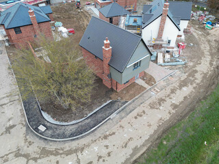Drone inspection view of a near completed detached private home of contemporary design. Seen near other homes of a British housing development site.