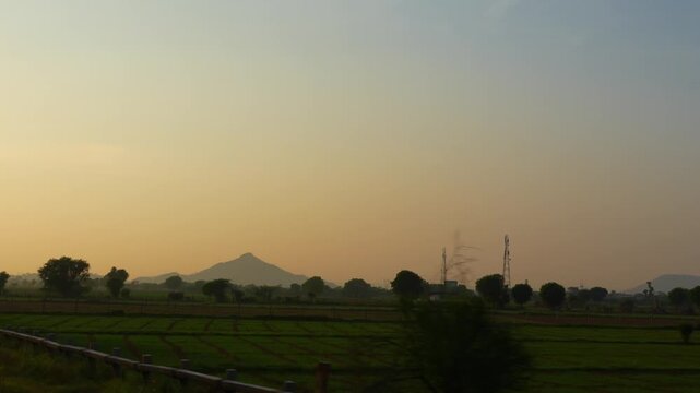A cinematic shot of an Indian train running parallel to the Aravalli Range during golden evening light. 