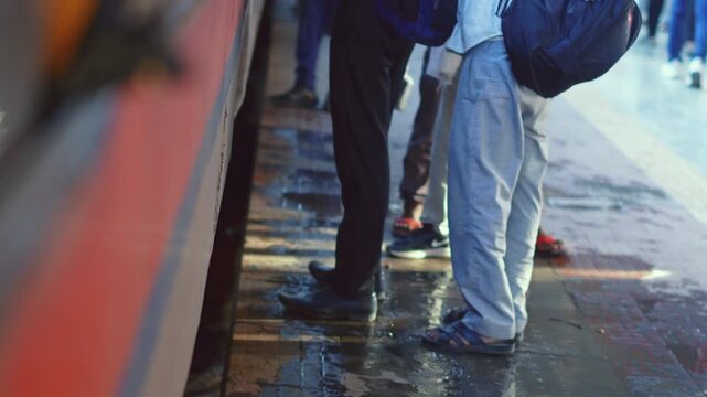 Close-up cinematic shot of people standing on a wet and dirty Indian railway platform beside a train.