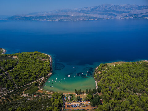 Aerial view of the verdant trees meeting the turquoise waters, where boats bob gently in a serene bay, Brac, Split-Dalmatia County, Croatia.