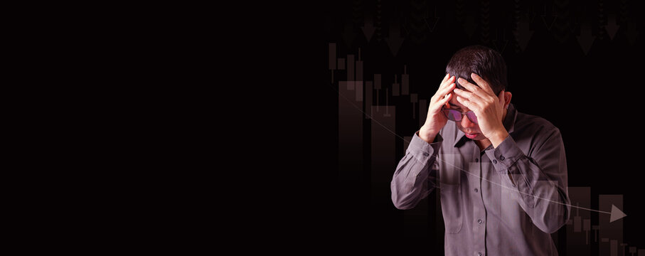 A worried businessman holding his head in frustration with a dark background and falling stock chart, symbolizing financial loss, market crash, or global economic recession.