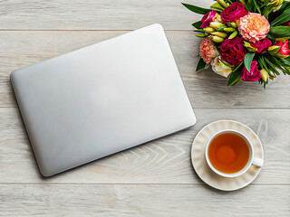 Top view of a closed laptop, cup of tea and flowers