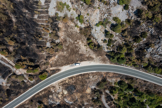 Aerial view of a winding road slicing through the rugged, rocky landscape, with burnt patches contrasting against the vibrant greenery, Biokovo, Republika Srpska, Bosnia and Herzegovina.