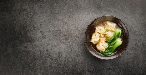 Wonton soup with bok choy in dark bowl on light background, top view copy space